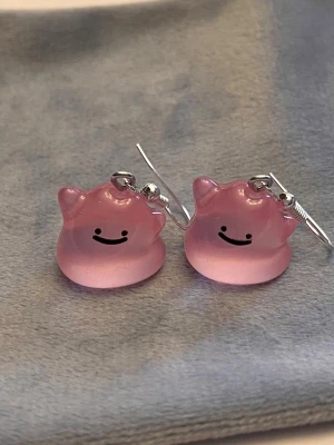 Självlysande Ditto örhängen Pokémon smycke  - Så gulliga örhängen med ljust rosa Ditto! Berlockerna är ca 1,5 x 1,5 cm. Den är också självlysande och lyser i mörkret.