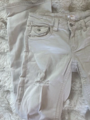 Vita bootcut jeans  - Säljer ett par vita jeans med klassisk femficksmodell och en snygg slitningar på benen. Jeansen är lågmidjade och är bootcut . Perfekta för dig som gillar en avslappnad och trendig stil.