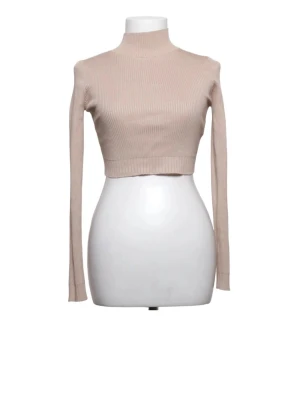 Beige croppad ribbad polotopp - Trendig croppad polotopp i beige med lång ärm och ribbad struktur. Perfekt för att styla med höga jeans eller kjol. Tidlös och enkel design som passar till många looks.