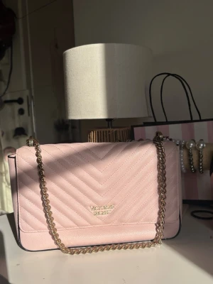 Ljusrosa Victoria’s Secret väska  - Fint skick både invändigt och utvändigt. Finns några små fläckar på undersidan och baksidan (syns på bilder) men i övrigt ser väskan knappt använd ut. Bandet går att ha dubbelt över axeln för kortare längd, men även längre till höft längd. 