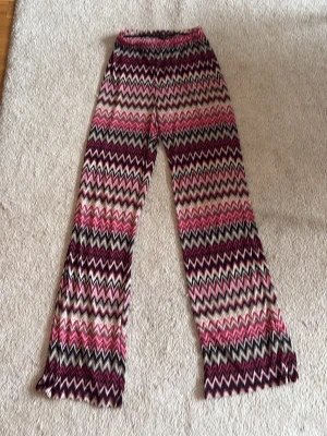 Mönstrade zigzag-leggings i rosa toner - Säljer ett par leggings med färgglatt zigzag-mönster i rosa, vinrött, svart och beige. De har en bekväm resår i midjan och är tillverkade i ett stretchigt material. Perfekta för dig som gillar att sticka ut med din stil!
