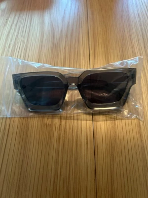 Svarta fyrkantiga solglasögon - Snygga solglasögon med bred, fyrkantig båge i transparent svart plast. Glasen är mörka och ger en cool och modern look. Perfekta för att lyfta din stil under soliga dagar.