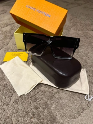 Svarta solglasögon - Säljer ett par statement solglasögon med stor, fyrkantig form och svarta bågar. Glasen är mörka och har en snygg gradient-effekt. Ikonisk detalj framtill. Kommer med originalfodral, putsduk och box.