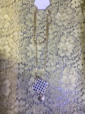 Guldigt halsband med fyrklöverhänge - Snyggt halsband i guldton med ett fyrklöverformat hänge dekorerat med små vita pärlor i rutmönster. Kedjan är tunn och elegant, och under hänget hänger en liten rund detalj. Perfekt accessoar för att lyfta din outfit.