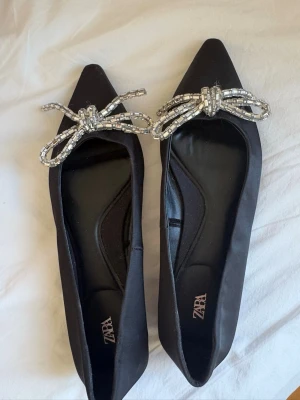 Super snygga ballerina skor - Snygga svarta ballerinaskor från Zara med spetsig tå och silvrig rosett💕använda en gång utomhus men säljer då de är för stora. Så skulle säga att de är normala i storleken då jag vanligtvis har 36 i skor