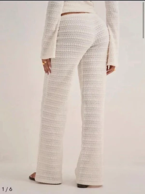 Vita stickade loungewear-byxor - Mysiga vita stickade loungewear-byxor med breda ben och låg midja. Byxorna har en mjuk och fluffig struktur som ger en avslappnad och trendig look. Perfekta för hemmamys eller chill dagar. Matcha gärna med en stickad tröja för en komplett outfit.