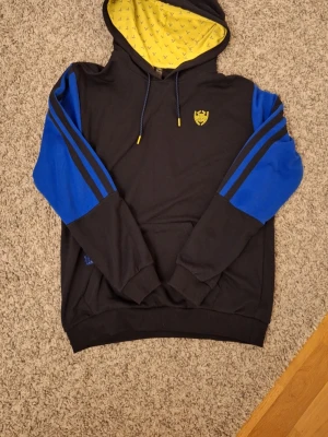 Marinblå Adidas 'Donovan Mitchell' hoodie - Snygg marinblå Adidas 'Donovan Mitchell' hoodie i storlek M med gula detaljer. Använd fåtal gånger och skicket är riktigt bra. Skick: 8/10