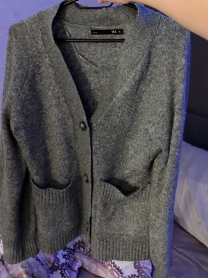 Grå kofta - Mysig grå kofta från H&M med knappar framtill och två stora fickor. Koftan är stickad i mjukt material och har ribbade muddar vid ärmslut och nederkant. Perfekt för lager-på-lager och enkel att matcha med olika outfits.