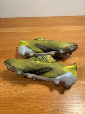 Gula Adidas X Speedflow fotbollsskor elite - Säljer ett par gula Adidas X Speedflow fotbollsskor med svarta och vita detaljer. Skorna har låg profil, snörning och ovandel i lätt syntetmaterial med texten FLUROSKIN på sidan. Sulan är designad för bra grepp på gräsplan. Perfekta för dig som vill ha speed på planen med bästa möjliga skomodell elite! En nackdel är ett minimalt hål i tån på högerskott och sliten nackdel i skon. Helt spelbara.