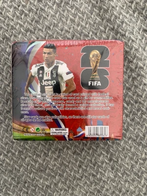 FIFA 2026 samlarkort fotboll - Box med samlarkort från FIFA 2026, med fotbollsstjärnor på framsidan. Förpackningen är röd med bilder på spelare i matchställ och FIFA-logga med VM-pokalen. Perfekt för dig som gillar fotboll och vill bygga din egen kortsamling.