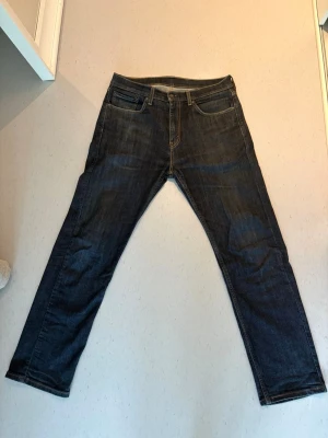 Mörkblå Levi's jeans straight fit - Säljer ett par klassiska mörkblå jeans från Levi's (505) med straight fit. Jeansen har fem fickor, gylf med dragkedja och knapp samt den ikoniska läderlappen bak i midjan. Tillverkade i slitstark denim med snygga kontrastsömmar. W32 L30
