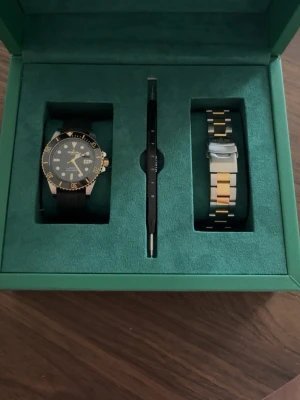 Marlow Miller datejust - Snygg klocka från marlow miller med svart urtavla och gulddetaljer. Setet innehåller ett  sportigt svart armband och ett extra armband i silver och guld. Kommer i en grön box och inkluderar verktyg för att byta armband. Inget kvitto tillkommer men säljes med prislapp från Åhléns. Använt en gång, helt nytt skick.