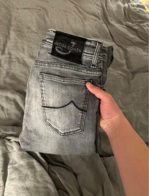 Grå slim fit jeans från Jacob Cohen - Snygga grå slim fit jeans från Jacob Cohen med klassisk femficksdesign och svart patch med logga bak. Jeansen har en tvättad look och smala ben, perfekta till en avslappnad stil. Tillverkade i mjukt denimtyg för skön känsla. W31 och modell 688.