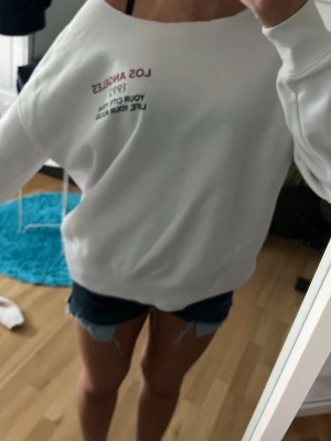Vit sweatshirt med Los Angeles-tryck - Säljer en vit sweatshirt med trycket 'Los Angeles 1992' i rött och svart på bröstet. Tröjan har rund halsringning och långa ärmar. Materialet är mjukt och skönt, perfekt för en avslappnad stil. Ingen huva. Passar dig som gillar streetwear och enkel design. Jag har klippt ringningen själv. 