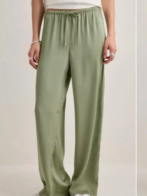 Gröna satin byxor med dragsko - Snygga satin byxor i grön färg med avslappnad passform och dragsko i midjan. Byxorna har raka ben och en mjuk, glansig yta som ger en lyxig känsla. Perfekta för chill dagar eller när du vill vara extra bekväm.