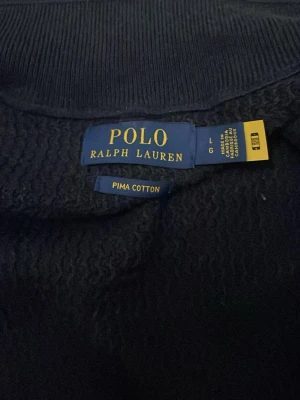 Mörkblå tröja från Polo Ralph Lauren - Mörkblå tröja från Polo Ralph Lauren i mjuk pima cotton. Klassisk design med rund hals och den ikoniska broderade loggan på bröstet. Perfekt för en stilren och avslappnad look.PRIS KAN DISKUTERAS 