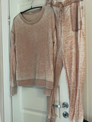  Beige loungewear-set i mjuk bomull - Mysigt loungewear-set i beige och ljusbrun melerad färg. Setet består av en långärmad tröja med rund hals och matchande byxor med dragsko och fickor. Tillverkat i mjuk och skön bomullsblandning, perfekt för avslappnade dagar hemma. Love and glamour 