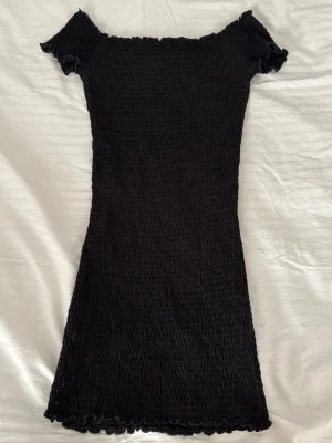 Svart smockad klänning Gina Tricot - Svart smockad kortklänning från Gina Tricot. Klänningen har offshoulder-modell med korta ärmar och vågig kant vid ärmslut och nederkant. 
