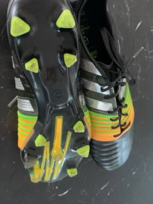 Adidas fotbollsskor Champions League. Slutat säljas - Snygga Adidas fotbollsskor med Champions League-design. Skorna är svarta med gröna och orange detaljer, silverfärgade ränder och svarta snören. Yttersulan har gröna dobbar och skon är tillverkad i syntetmaterial för bästa grepp och komfort på planen. Skorna elit modellen och det har slutat säljas. Pris kan diskuteras!