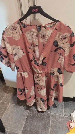 Blommig omlottklänning från SHEIN Curve - Supersöt kort blommig klänning från SHEIN Curve i rosa med stora vita och beige blommor. Klänningen har omlottmodell, v-ringning och korta ärmar. Perfekt för vår och sommar, med en luftig och bekväm passform.