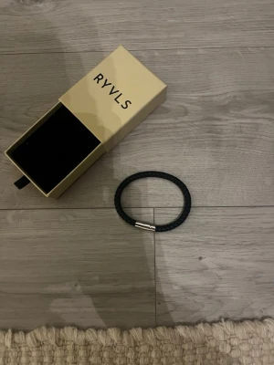 Svart flätat armband från RYVLS - Stilrent svart armband från RYVLS i flätat läder med ett snyggt magnetlås i silverfärgad metall. Perfekt accessoar för att lyfta din outfit med en modern och enkel touch. Levereras i originalask.