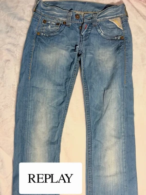 Ljusblå jeans från Replay - Säljer ett par ljusblå jeans från Replay med klassisk femficksmodell och snygga slitningar framtill. Jeansen har raka ben och detaljerade bakfickor med Replay-logga. 