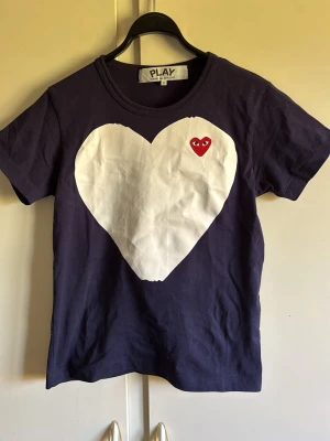 Mörkblå Comme des CARGONS Tshirt - Tja, säljer nu en riktigt schysst och populär mörkblå t-shirt från Comme des CARGONS  PLAY i storlek S  med ett stort vitt hjärta och en röd hjärtdetalj med ögon på bröstet. Klassisk rund hals och korta ärmar. Tillverkad i mjuk bomull. Använd ett fåtal gånger och inget fel på den alls! Hör av er vid funderingar😁