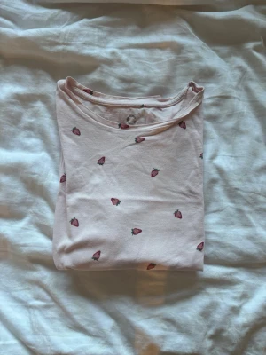Ljusrosa pyjamas med jordgubbstryck - Supersöt ljusrosa t-shirt och shorts från Cubus med små jordgubbar tryckta över hela plagget.