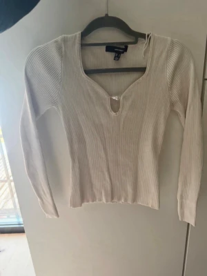 Ribbad beige långärmad topp VERO MODA - Trendig ribbad topp i beige från VERO MODA med lång ärm och djup v-ringning med liten cut-out detalj framtill. Perfekt att styla med jeans eller kjol för en snygg look.