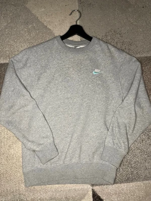 Nike sweatshirt - Grå stickad sweatshirt från Nike med broderad logga i vitt och ljusblått på bröstet. Klassisk rund halsringning och ribbade muddar vid ärmslut och nederkant. Perfekt för en chill och sportig stil.