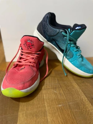 Färgglada sneakers från Puma x Kool-Aid - Unika sneakers från Puma x Kool-Aid med en sko i rött och en i turkosblått. Båda har mesh-ovandel, snörning och en cool Kool-Aid-figur på plösen. Sulan är vit med limegrön detalj. Perfekt för dig som vill sticka ut med färg och lekfull design.