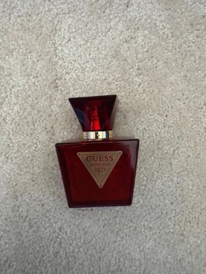 Guess Seductive Red parfym - En elegant parfym från Guess, Seductive Red, i en djup röd glasflaska med guldiga detaljer och en geometrisk form. Flaskan har en bred, kantig kork och en triangelformad etikett framtill. Perfekt för dig som gillar lyxiga och moderna dofter. Parfymen är i 30ml.