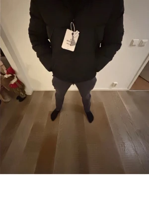 Svart dunjacka från Moncler - Säljer en svart dunjacka från Moncler med tydlig logga på insidan av dragkedjan. Jackan har en klassisk puffer-modell, hög krage och två sidofickor. Perfekt för kalla vinterdagar och riktigt snygg till streetwear-stilen.