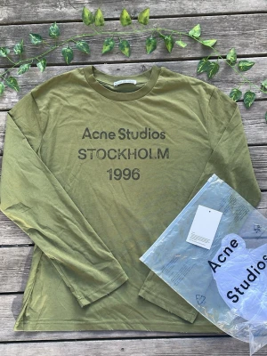  Acne Studios long sleeve  - Tja! Jag säljer en Olivgrön långärmad topp från Acne Studios med tryck 'Acne Studios STOCKHOLM 1996' på bröstet. Rund halsringning och rak passform. Tillverkad i mjuk bomull, perfekt för en avslappnad och trendig look.