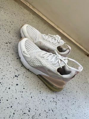 Nike Air Max 270 vita/rosa sneakers - Nike Air Max 270 sneakers i vitt med ljusrosa detaljer. Använda men fortfarande vita och fräscha. Bilden e lite ghetto men tog den på balkongen:)  