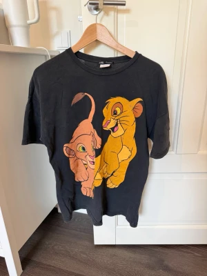 Svart Lejonkungen t-shirt med tryck - Svart t-shirt från Zara med stort färgglatt Lejonkungen-tryck framtill. Klassisk rund hals och korta ärmar. Perfekt för dig som älskar Disney och vill ha en avslappnad och cool stil.