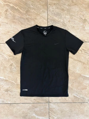 Svart Nike Dri-FIT t-shirt - Svart sportig t-shirt från Nike med Dri-FIT-teknologi som håller dig torr under träningen. T-shirten har rund hals, korta ärmar och diskret Nike-logga på bröstet samt tryck på ena ärmen. Perfekt för gymmet eller löprundan.