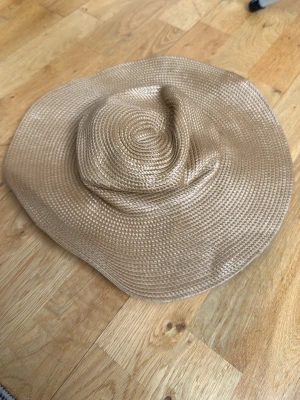 Beige solhatt från H&M - Säljer en beige solhatt från H&M med bred, vågig brätte. Hatten är tillverkad i flätad polyester och har en klassisk strandstil. Perfekt accessoar för soliga dagar och ger en chill vibe till din outfit.