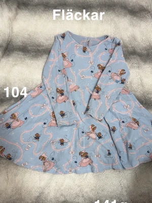 Blå långärmad klänning med disneymotiv - Söt blå långärmad klänning med disneytryck med rosa detaljer. Klänningen har rund hals och ett svängigt kjolparti. Perfekt för dig som gillar lekfulla mönster och mjuka material.🌸 Fläckar. Storlek 104