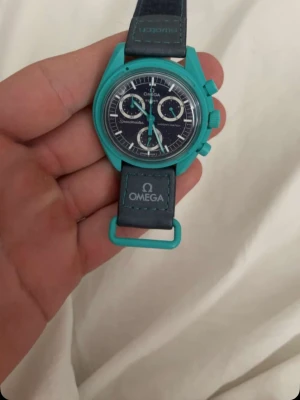 Omega klocka - Säljer en Omega x Swatch Speedmaster med turkos boett och svart urtavla. Klockan var tyvärr tappat siffrorna utanför klockan som ni kan se men annars fint skick 