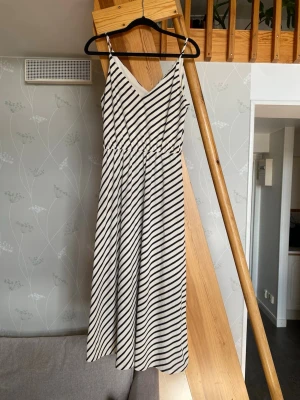 Randig midiklänning med smala axelband strl XS - Snygg långklänning med svarta och vita diagonala ränder, v-ringad och med smala axelband. Klänningen har en avslappnad passform och är perfekt för varma dagar. Tillverkad i ett mjukt och lätt material som känns skönt mot huden.