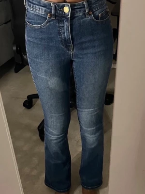 Blå bootcut jeans med hög midja - Säljer ett par blå bootcut jeans med hög midja och klassiska fem fickor. Perfekta för en trendig och avslappnad look. Tyvärr har de fått en klorin fläck.