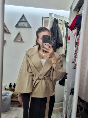 Beige kappa - Säljer en trendig jätte fin beige kappa från Gina Tricot med bred krage och knytbälte i midjan. Kappan har en loose passform och vida ärmar som ger en avslappnad look. Perfekt för lager-på-lager och enkel att styla till olika outfits. Säljer eftersom jag har för många jackor och kappor. Använd endast en gång. Ny pris 600kr