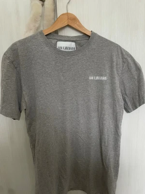 Grå t-shirt från Han Kjøbenhavn - Snygg grå t-shirt från Han Kjøbenhavn med minimalistisk vit logga på bröstet. Klassisk rak passform och rund halsringning. Tillverkad i mjukt bomullsmaterial som känns skönt mot huden. Perfekt basplagg för en clean och stilren look.