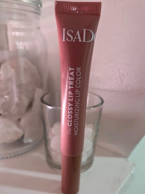 Isadora Glossy Lip Treat Ginger Glaze - Glansigt läppglans från Isadora i färgen Ginger Glaze, en mjuk rosa-brun nyans. Tuben är smidig och lätt att ta med, och formulan är återfuktande med ingredienser som olivolja och sheasmör. Perfekt för dig som vill ha glansiga och återfuktade läppar.