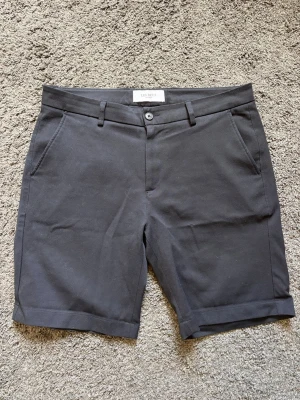 Svarta shorts från Les Deux - Stilrena svarta shorts från Les Deux med klassisk passform. Shortsen har bälteshällor, knapp och dragkedja framtill samt två sidofickor och två bakfickor. Perfekta för sommaren och passar till det mesta. Nypris 1099kr.