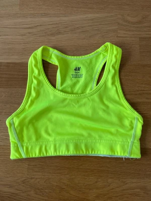 Neongul sport-bh från H&M - Sport-bh i neongult från H&M med brottarrygg och bred resår nedtill. Tillverkad i stretchigt funktionsmaterial som andas, perfekt för träning och sportaktiviteter. Snygg och bekväm passform som ger bra stöd.