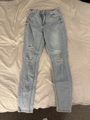 Ljusblå ripped skinny jeans - Säljer ett par ljusblå skinny jeans med slitningar och hål på framsidan. Jeansen har fickor, hög midja och är tillverkade i stretchigt denimtyg för en bekväm passform. Endast prövade men aldrig använda.