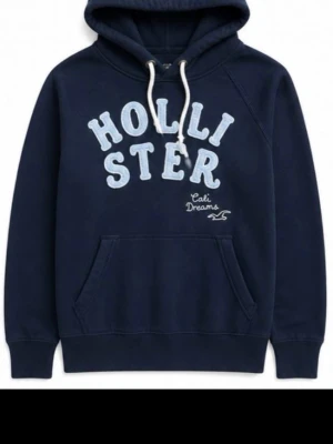 Mörkblå hoodie från Hollister - Mörkblå hoodie från Hollister med stor vit logga och texten 'Cali Dreams' framtill. Klassisk känguruficka, huva med vita snören och mjukt material. Perfekt för en avslappnad och cool stil.