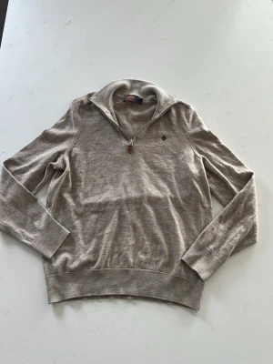 Beige stickad tröja från Morris - Beige stickad tröja från Morris i 100% merinoull. Tröjan har halv dragkedja vid kragen, långa ärmar och ribbade muddar. Perfekt för lager-på-lager och snygg till jeans eller chinos. Finns inga defekter på tröjan utifrån det jag ser. Tröjan är i storlek M men passar som en S-XS. Priset är ej hugget i sten.